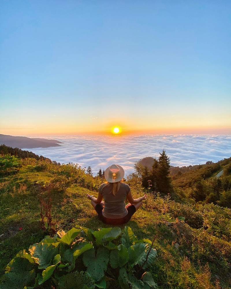 Sunset over a sea of clouds, a person sitting on a slope in Gomismta