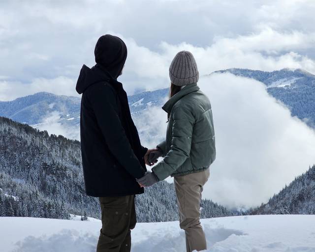 A couple with their backs to the camera, looking at clouds over the mountains