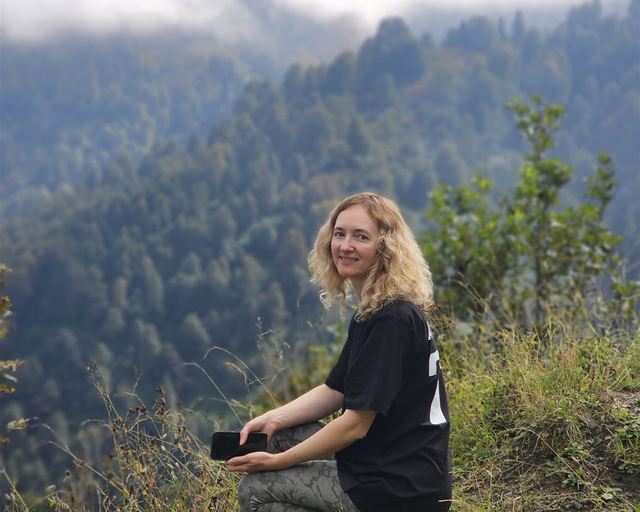 A woman on a grassy slope above a misty forest