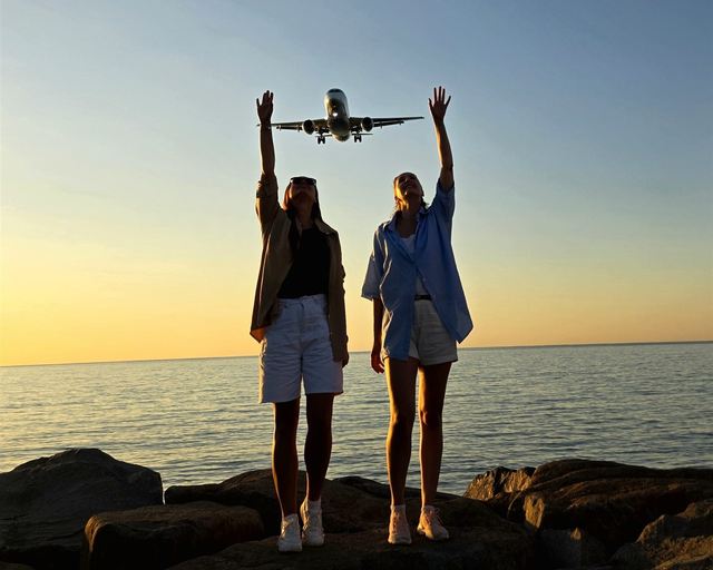 Two women reaching toward a plane above the sea at sunset