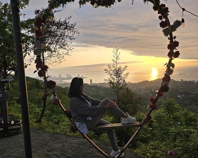 A woman on a heart-shaped swing above the coast at sunset