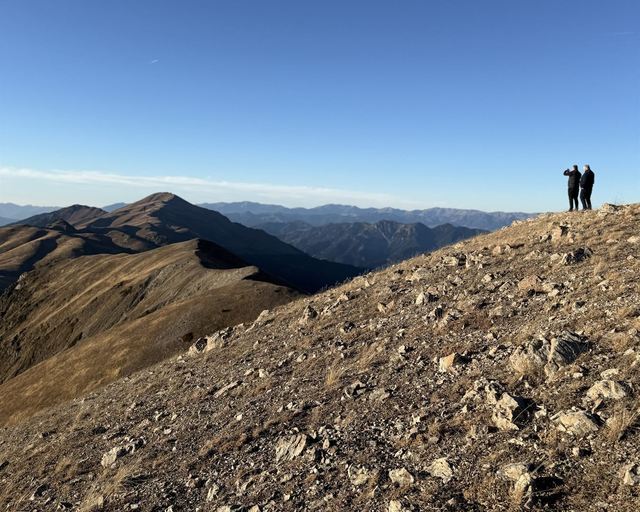 Two people on a ridge above mountain slopes