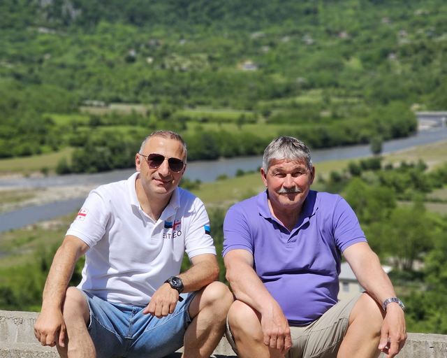 Two guests sitting with a mountain valley and river behind them