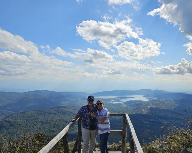 A couple on a viewing platform above a lake and the Racha mountains